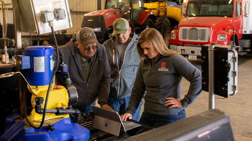 A University researcher discussed data with two farmers in a machine shed.